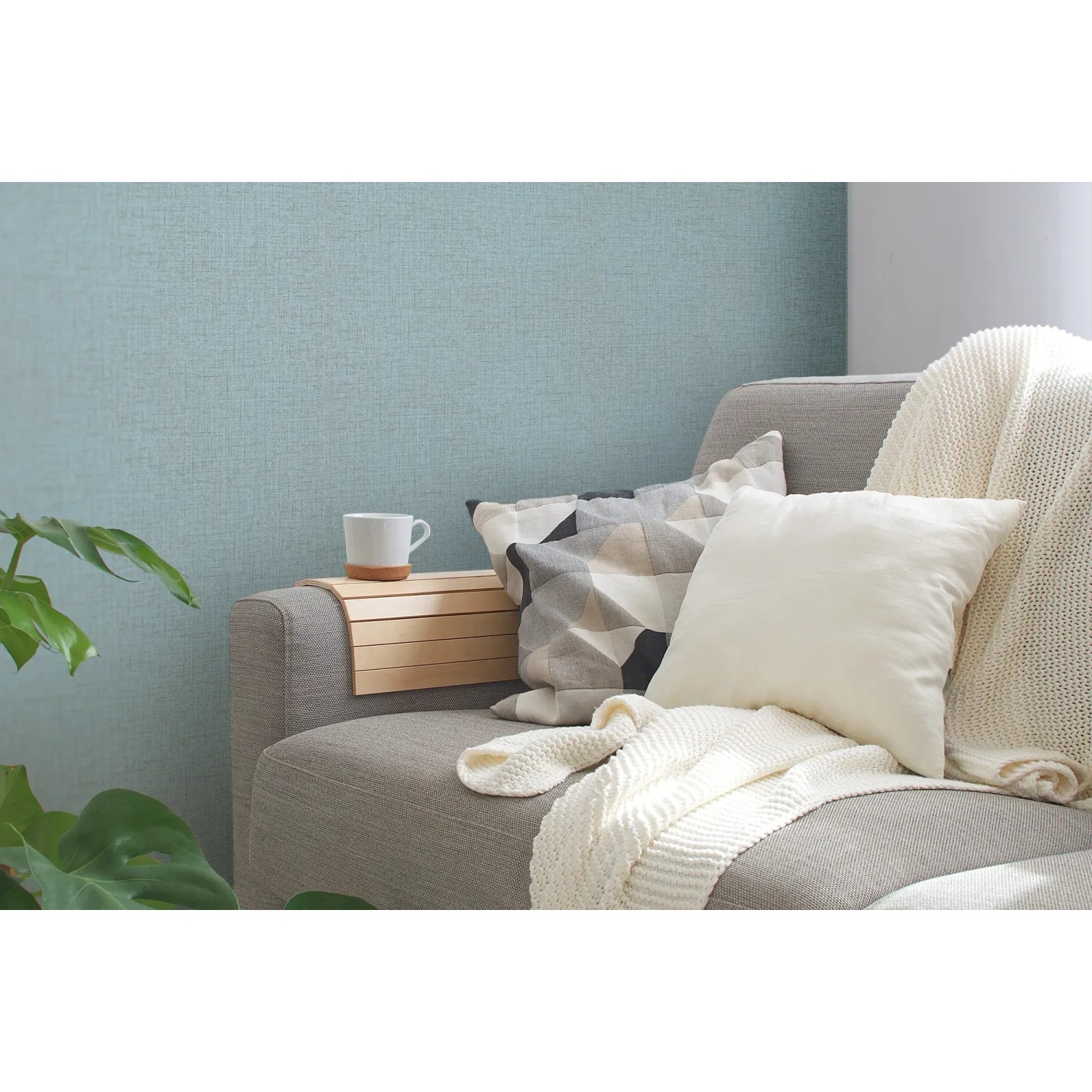Blaue Vliestapete mit leichter Struktur an Wand hinter Sofa mit Kissen und Decke.