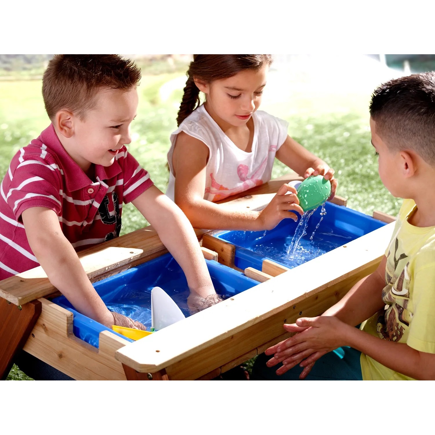 Kinder spielen am Axi Sand- und Wasser-Picknicktisch Nick mit blauen Wannen und Sonnenschirm.