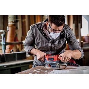 Mann schleift Holz mit dem roten Einhell TE-BS 850 E Bandschleifer. Inklusive Staubabsaugung.