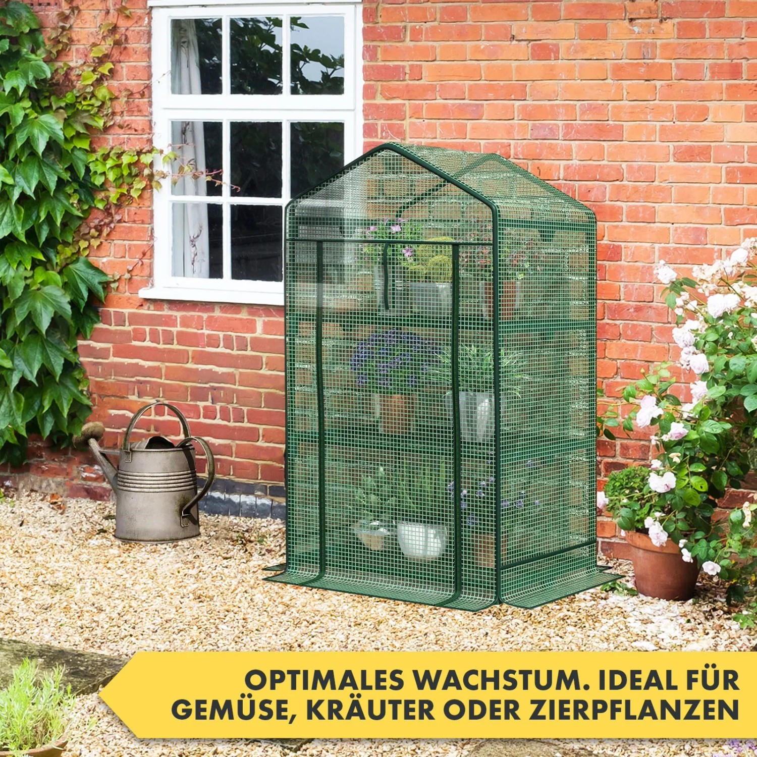 Kompaktes, grünes KARAT Gewächshaus Bloom mit 2 Ebenen und Pflanzen vor einer Backsteinmauer.