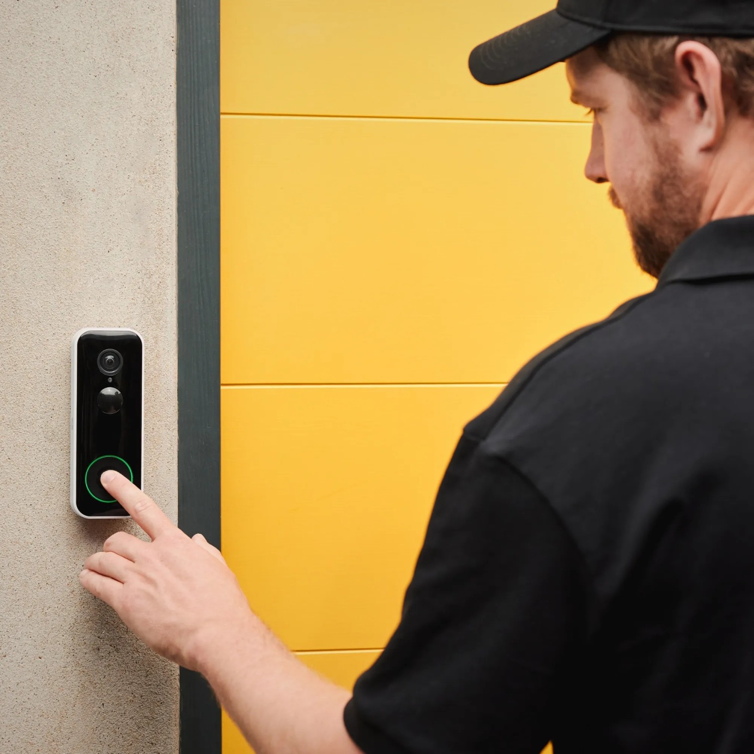 Mann betätigt Yale Smart-Camera Türklingel (Full HD, Akku, WLAN) an grauer Wand neben gelber Tür.