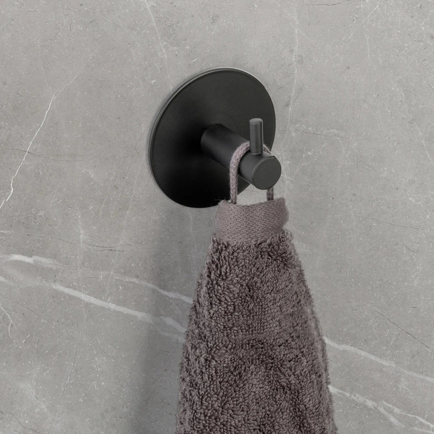 Schwarzer Schöner Wohnen Wandhaken Uno Meleto mit Handtuch an grauer Wand.