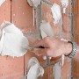 Ansetzgips Knauf Perlfix wird mit einer Kelle auf eine Ziegelwand aufgetragen.