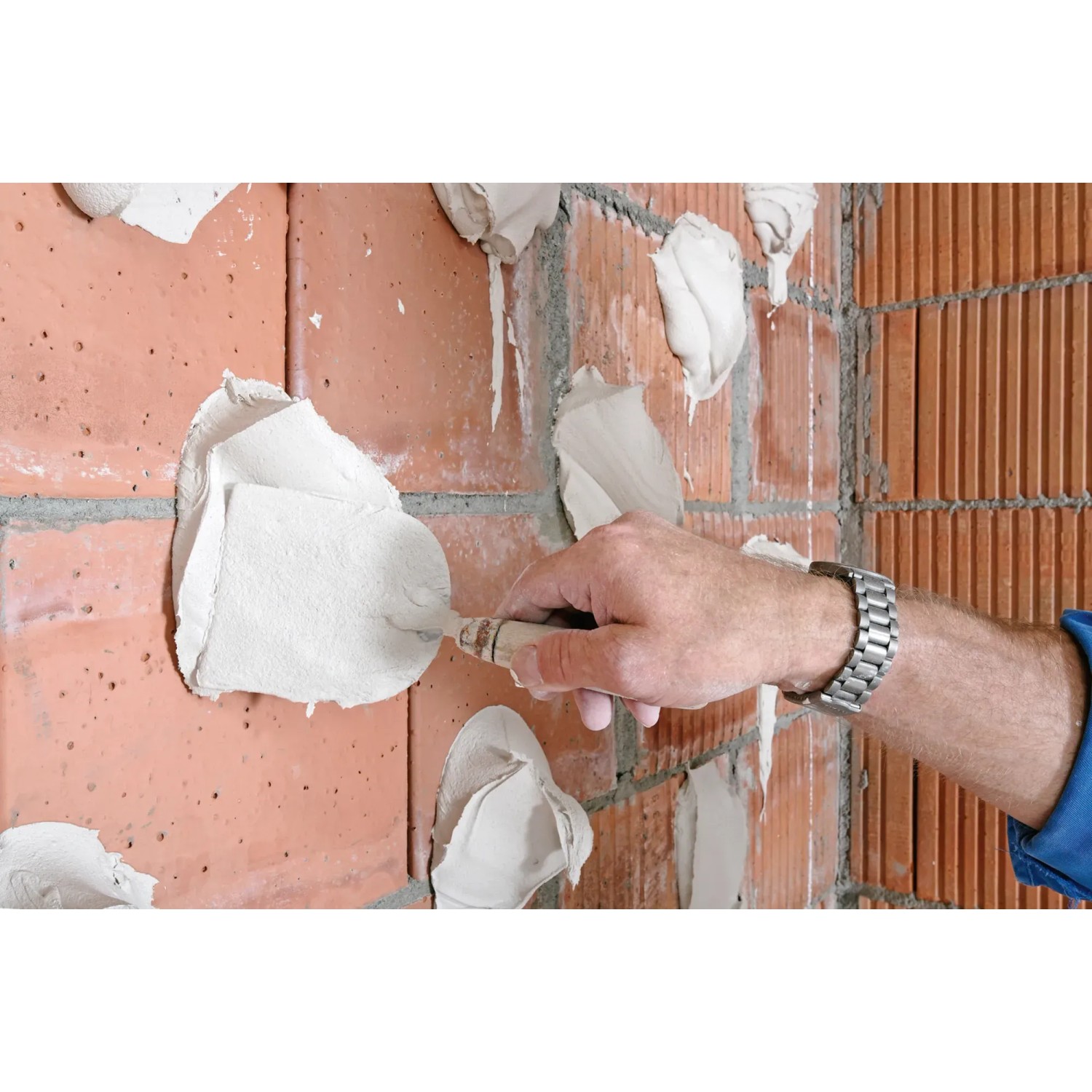 Ansetzgips Knauf Perlfix wird mit einer Kelle auf eine Ziegelwand aufgetragen.