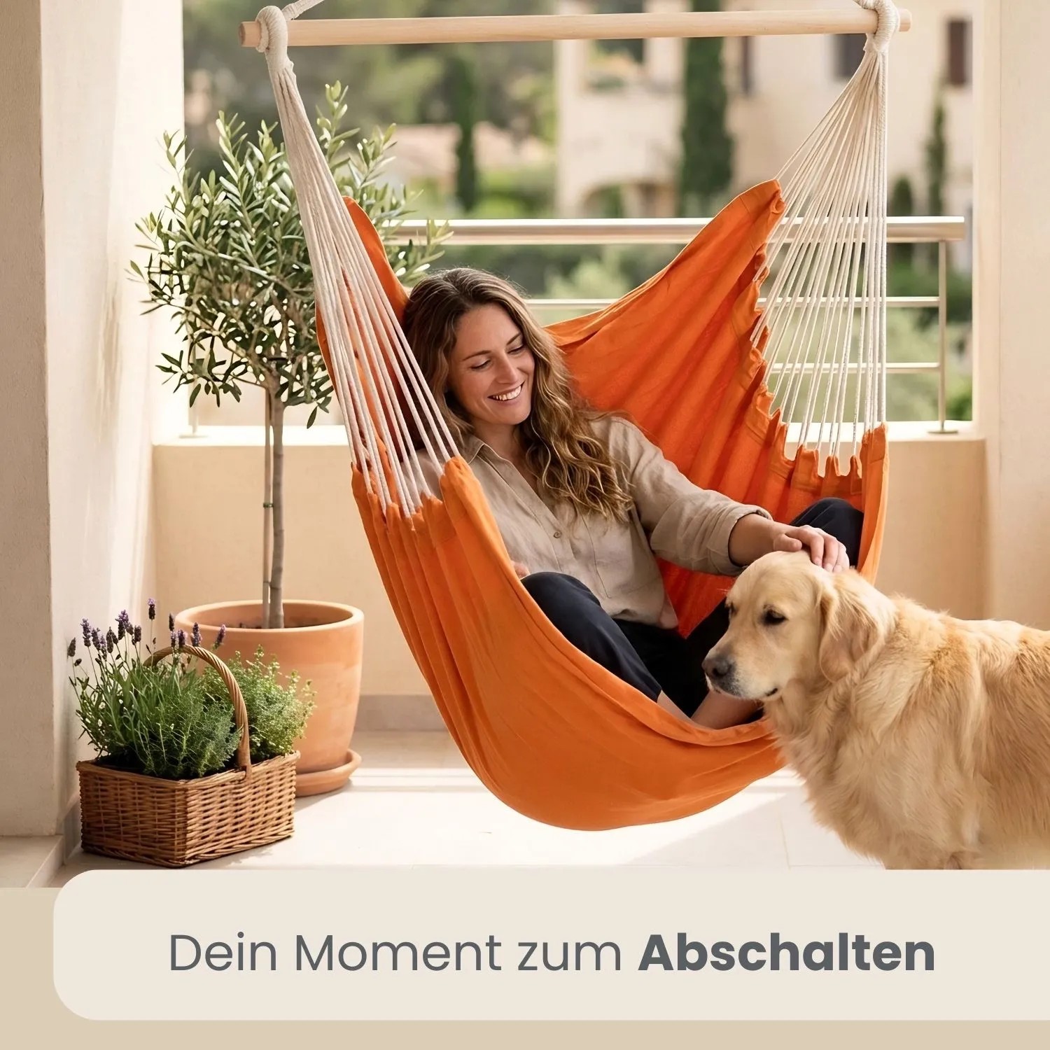 Orangefarbener AMANKA Hängesessel mit Frau und Hund auf Balkon. Bequemer Baumwoll-Schwebesessel für Entspannung.