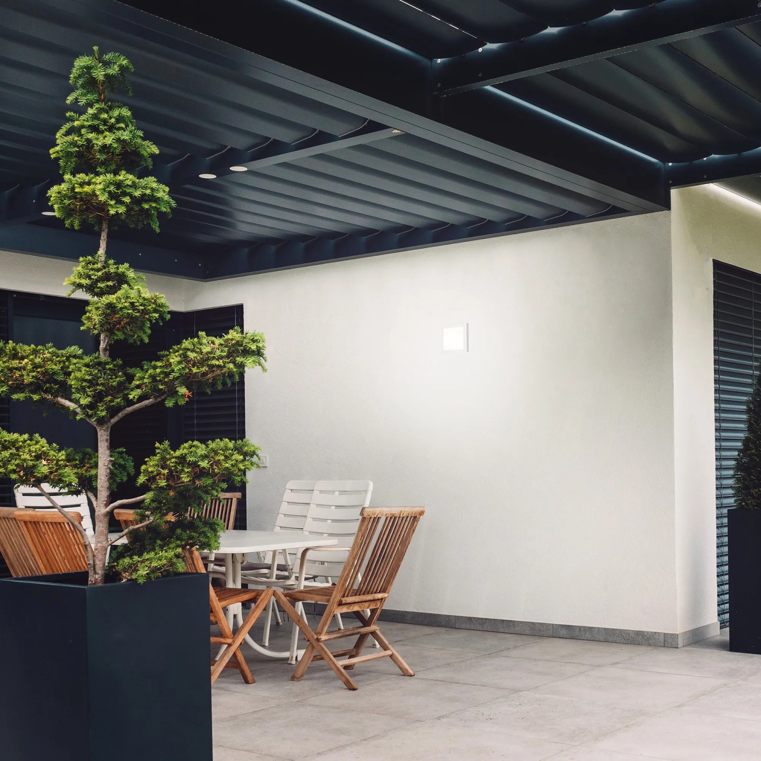 Eckige, weiße Brilo LED-Außenleuchte Frankfurt an Hauswand über Terrasse mit Sitzgruppe.
