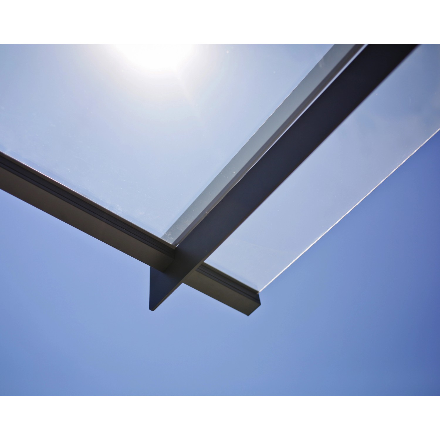 Palram Canopia Vordach Nancy, anthrazitfarbenes Gestell mit klarer Platte vor blauem Himmel.