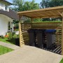 Weka Unterstellplatz Größe 2 aus Holz mit drei Mülltonnen vor einem Haus.