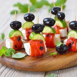 Holz-Zahnstocher halten bunte Tapas-Spieße mit Oliven, Gurke, Paprika und Käse auf einem Holzbrett.