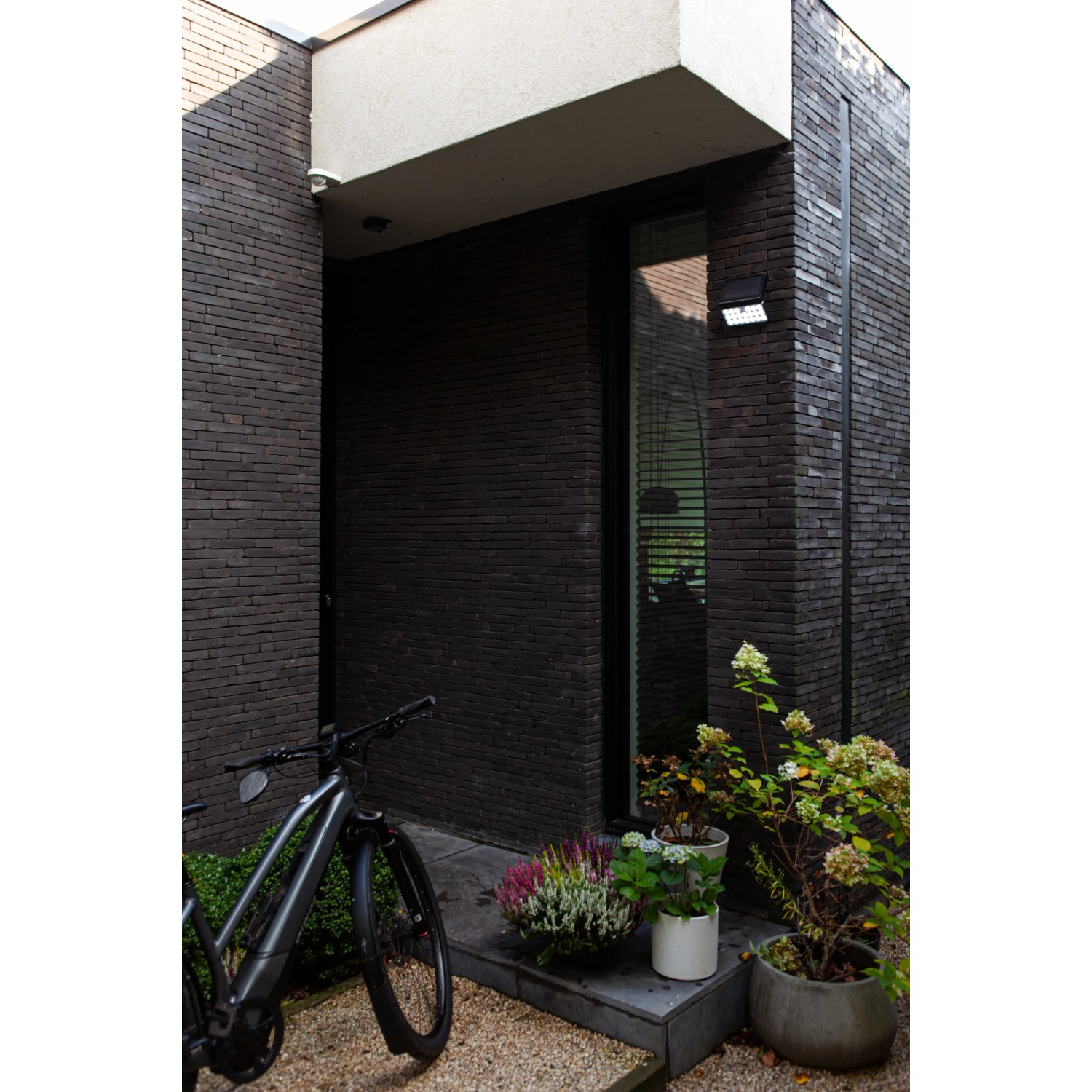 Schwarze Lutec LED Solar-Wandleuchte Tuda mit Bewegungsmelder an dunkler Hauswand.