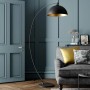 Schwarze Lindby Bogenleuchte Jonera mit goldenem Lampenschirm im Wohnzimmer.
