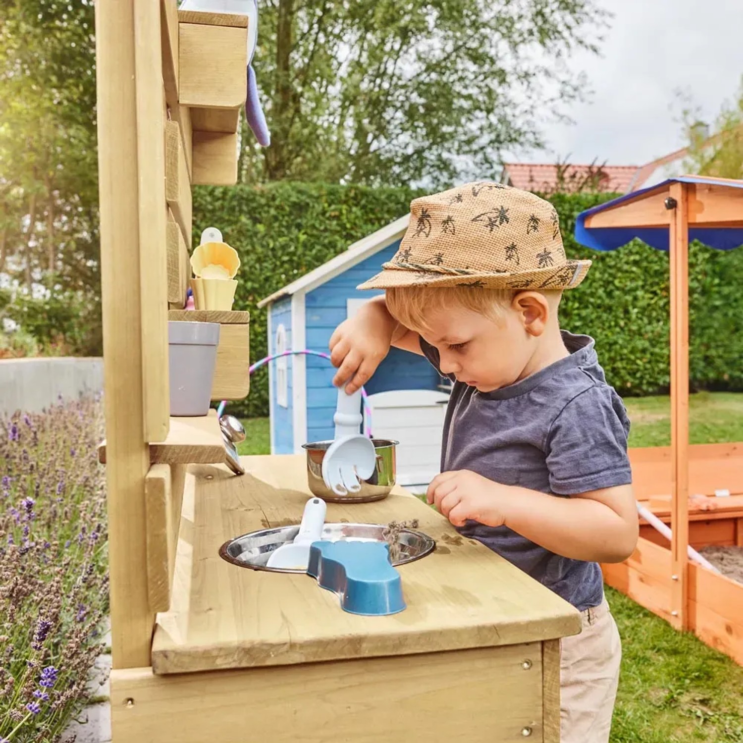 Kind spielt mit der Home Deluxe Spielküche Mandu im Garten mit Zubehör.
