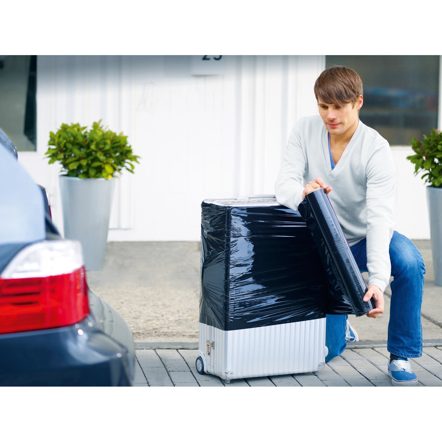 Mann verpackt Koffer mit schwarzer LUX Stretchfolie für Umzug oder Transport.