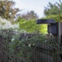 Anthrazitfarbene Lutec Solar-Wandleuchte Diso mit Bewegungsmelder an Holzzaun im Garten.