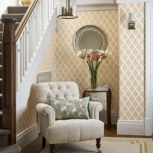 Laura Ashley Vliestapete Florin Gold im Raum, mit Sessel und Deko. Elegante, goldene Dekorative Tapete.