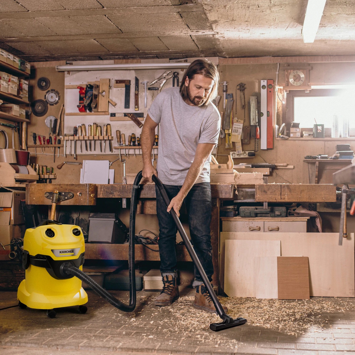 Mann saugt mit gelbem Kärcher WD 4 V-20/5/22 Nass-Trockensauger Späne in Werkstatt.