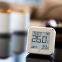 Shelly Temperatur Sensor Plus H&T G3 in Hellbeige auf Tisch mit Anzeige von Temperatur und Luftfeuchtigkeit.