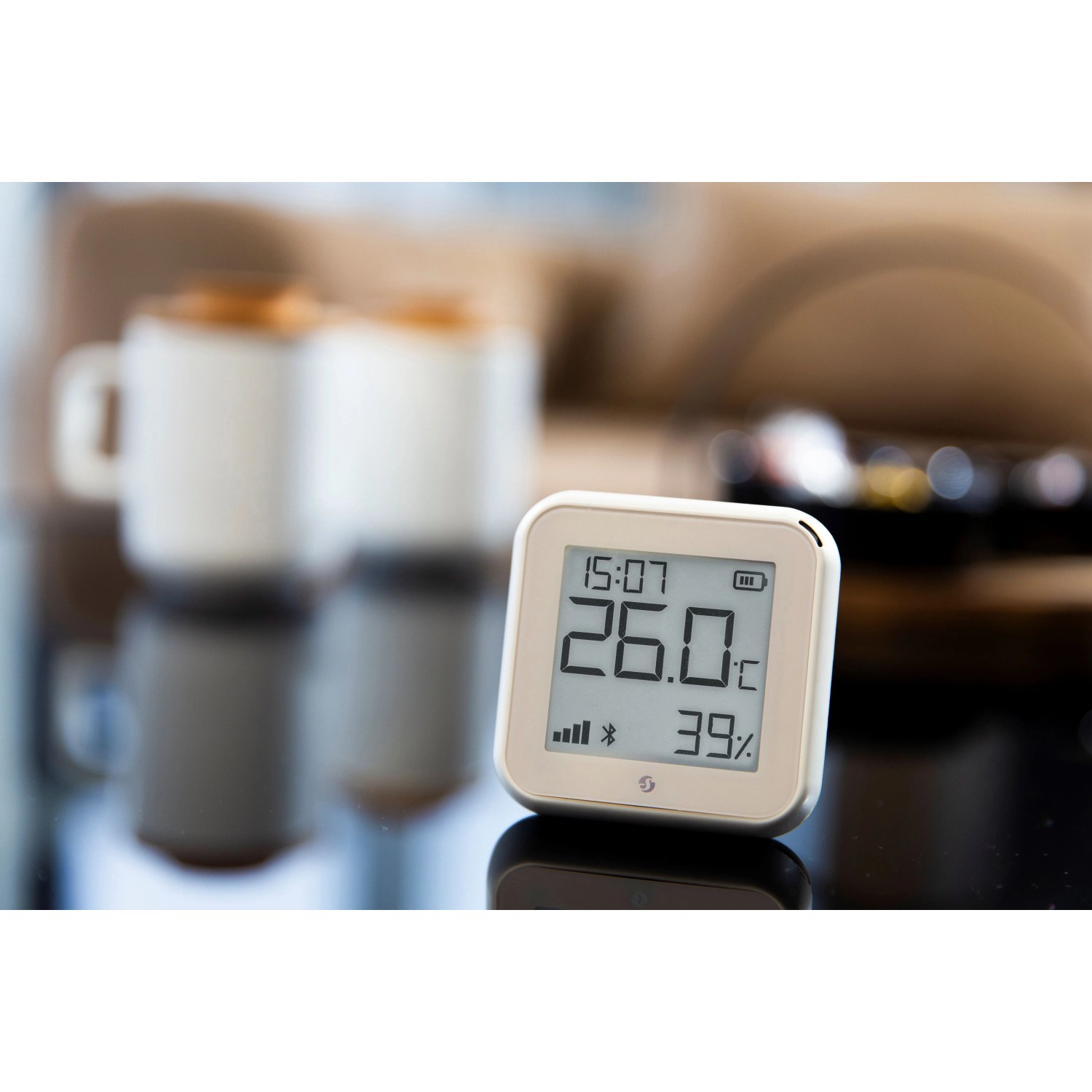 Shelly Temperatur Sensor Plus H&T G3 in Hellbeige auf Tisch mit Anzeige von Temperatur und Luftfeuchtigkeit.