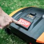 Hand drückt Stopptaste am Yard Force EasyMow 260B Mähroboter auf Rasen.