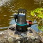 Gardena Schmutzwasser-Tauchpumpe 9000 auf Stein vor Teich, mit blauem Zierstreifen.
