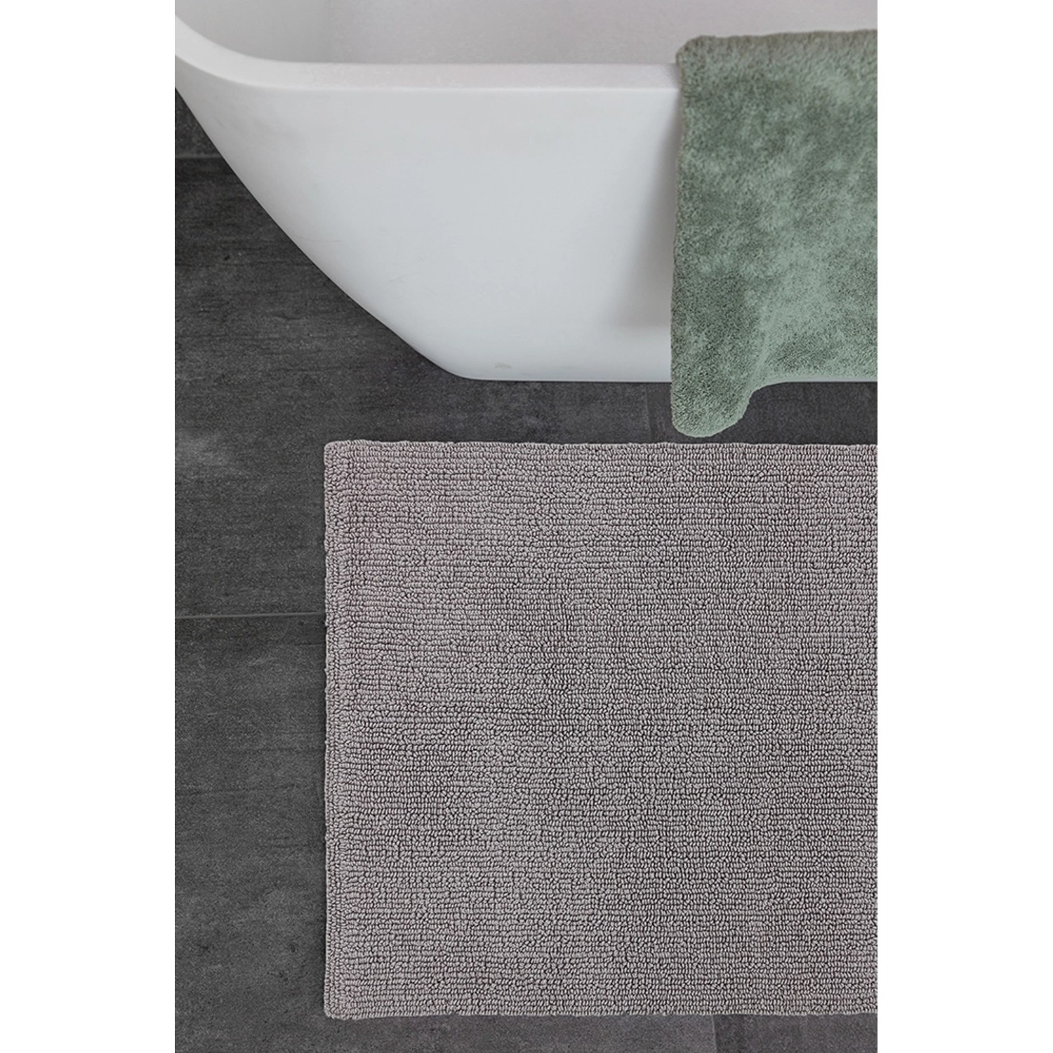 Schöner Wohnen Badteppich Bahamas, 60x90 cm, hellgrau, vor Badewanne auf dunklen Fliesen.