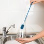 Wenko Silikon Flaschenbürste in Blau reinigt eine Karaffe in der Spüle.