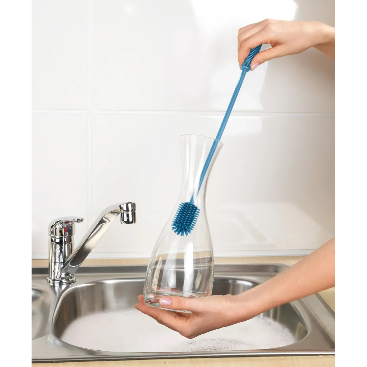 Wenko Silikon Flaschenbürste in Blau reinigt eine Karaffe in der Spüle.