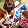 Kinder spielen am Axi Nick Sand- und Wasser-Picknicktisch aus Holz mit blauen Behältern.