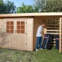 OBI Holz-Gartenhaus La Spezia mit Anbaudach und Person beim Hineinstellen einer Mülltonne.
