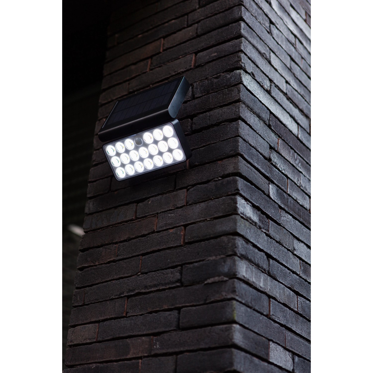 Schwarze Lutec LED Solar-Wandleuchte Tuda mit Bewegungsmelder an Backsteinwand.
