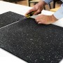 Zuschnitt einer schwarzen KARAT Antivibrationsmatte / Schallschutzmatte mit Cutter auf einer weißen Oberfläche.