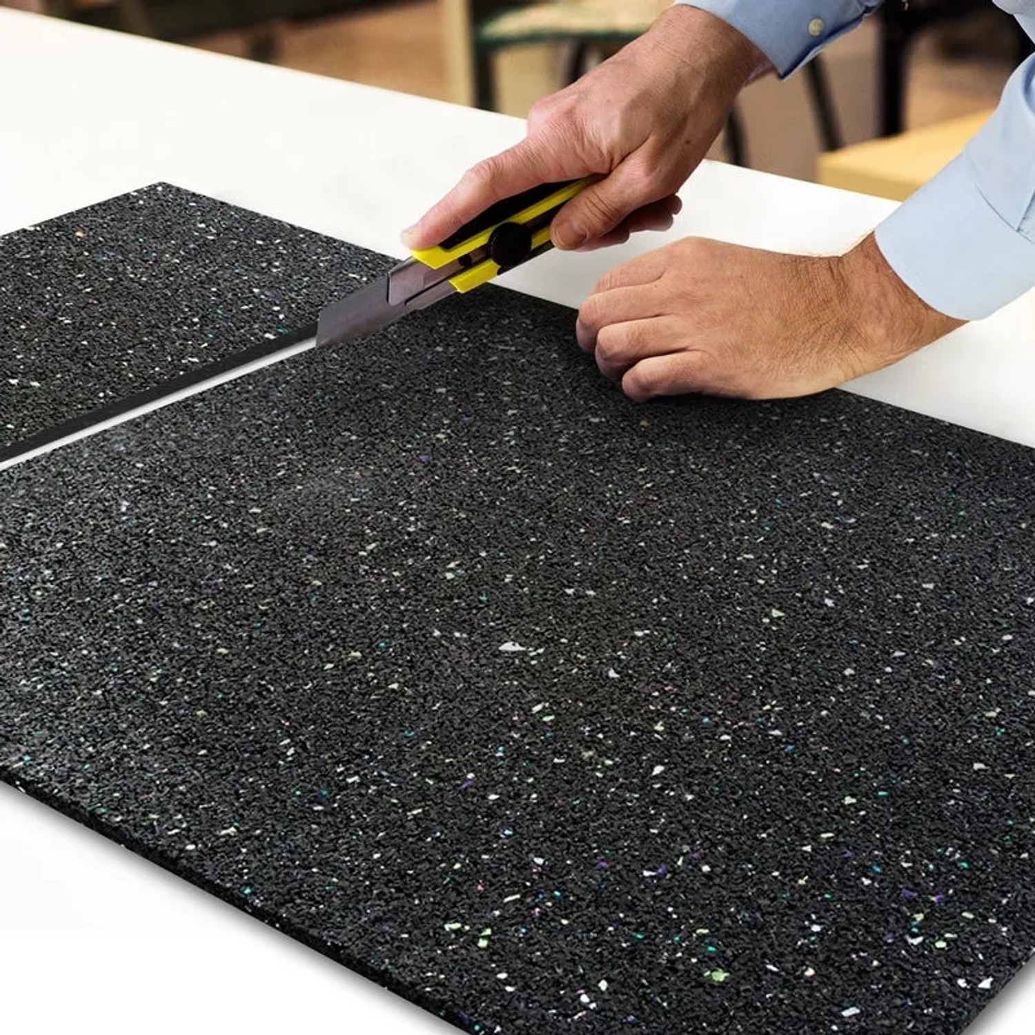 Zuschnitt einer schwarzen KARAT Antivibrationsmatte / Schallschutzmatte mit Cutter auf einer weißen Oberfläche.