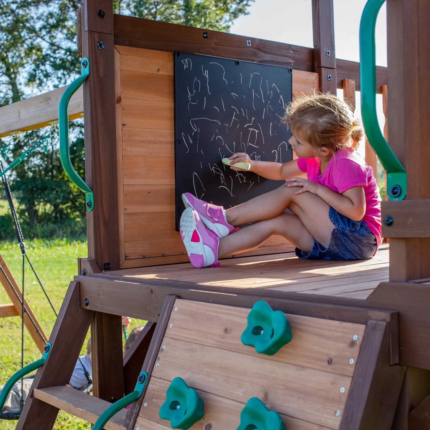 Kind malt mit Kreide auf der Tafel des Backyard Discovery Spielturms Cedar Cove.