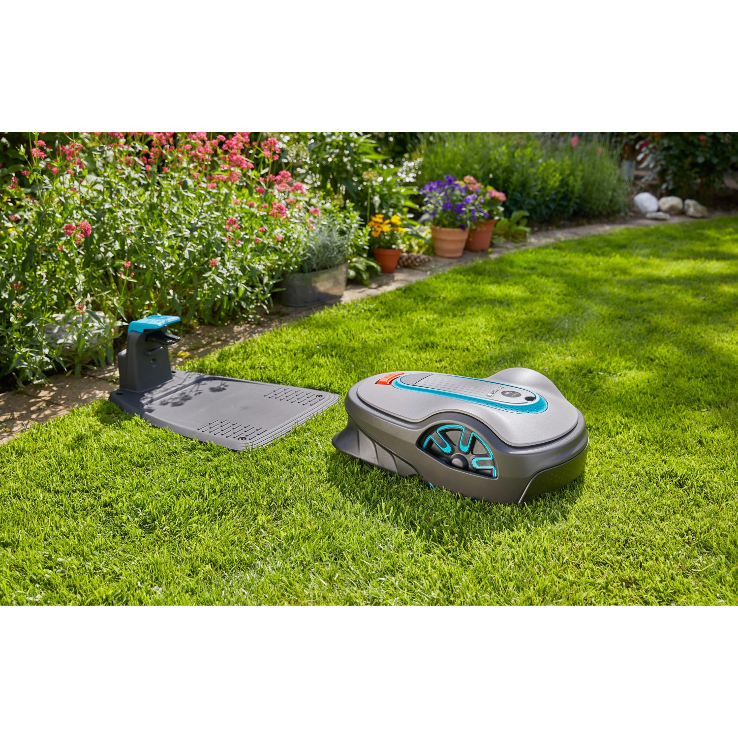 Gardena smart Sileno life Mähroboter Set mit Ladestation auf Rasen vor Blumenbeet.
