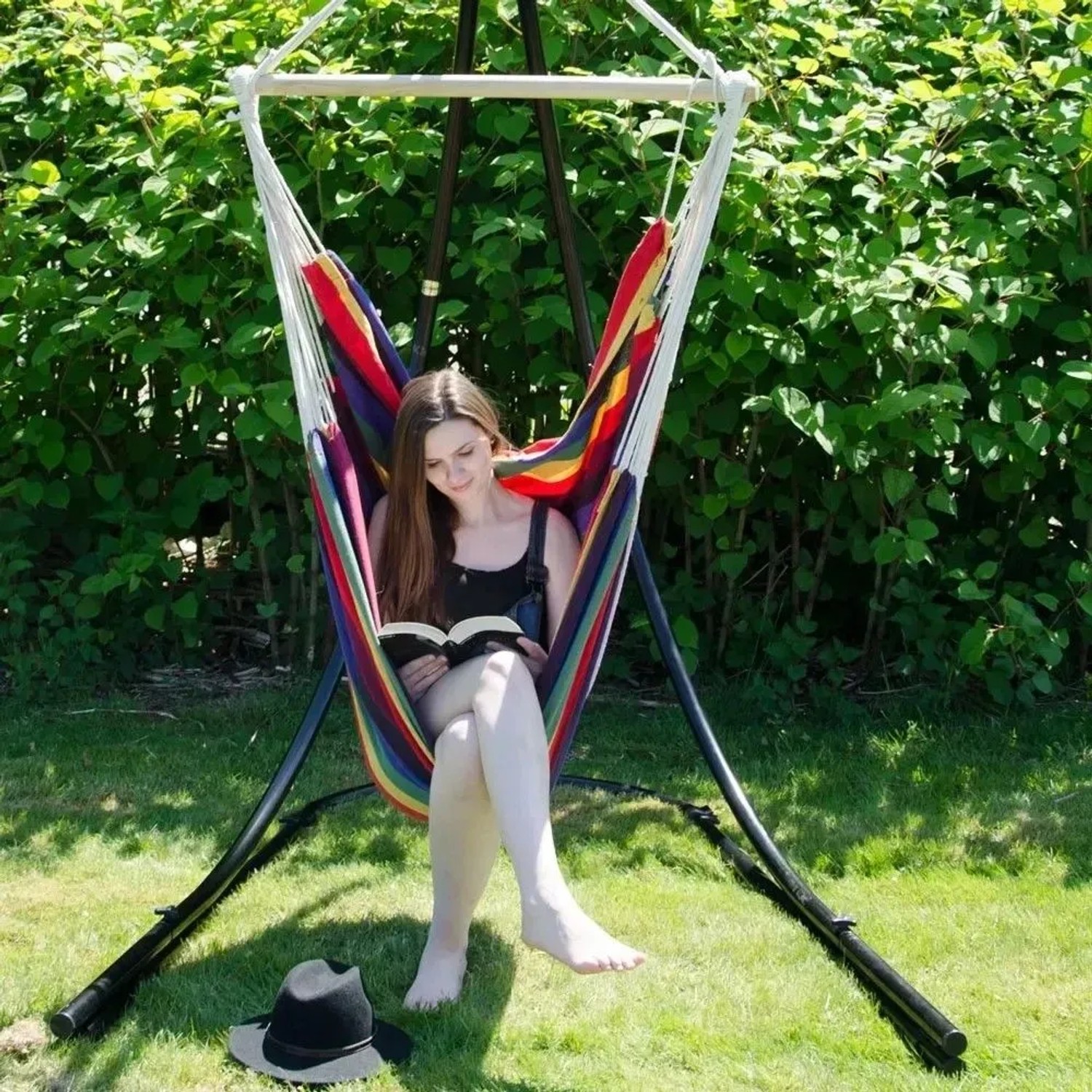 Frau liest entspannt in einem bunten AMANKA Hängesessel mit Holzstab im Garten. Ideal für Outdoor & Indoor.