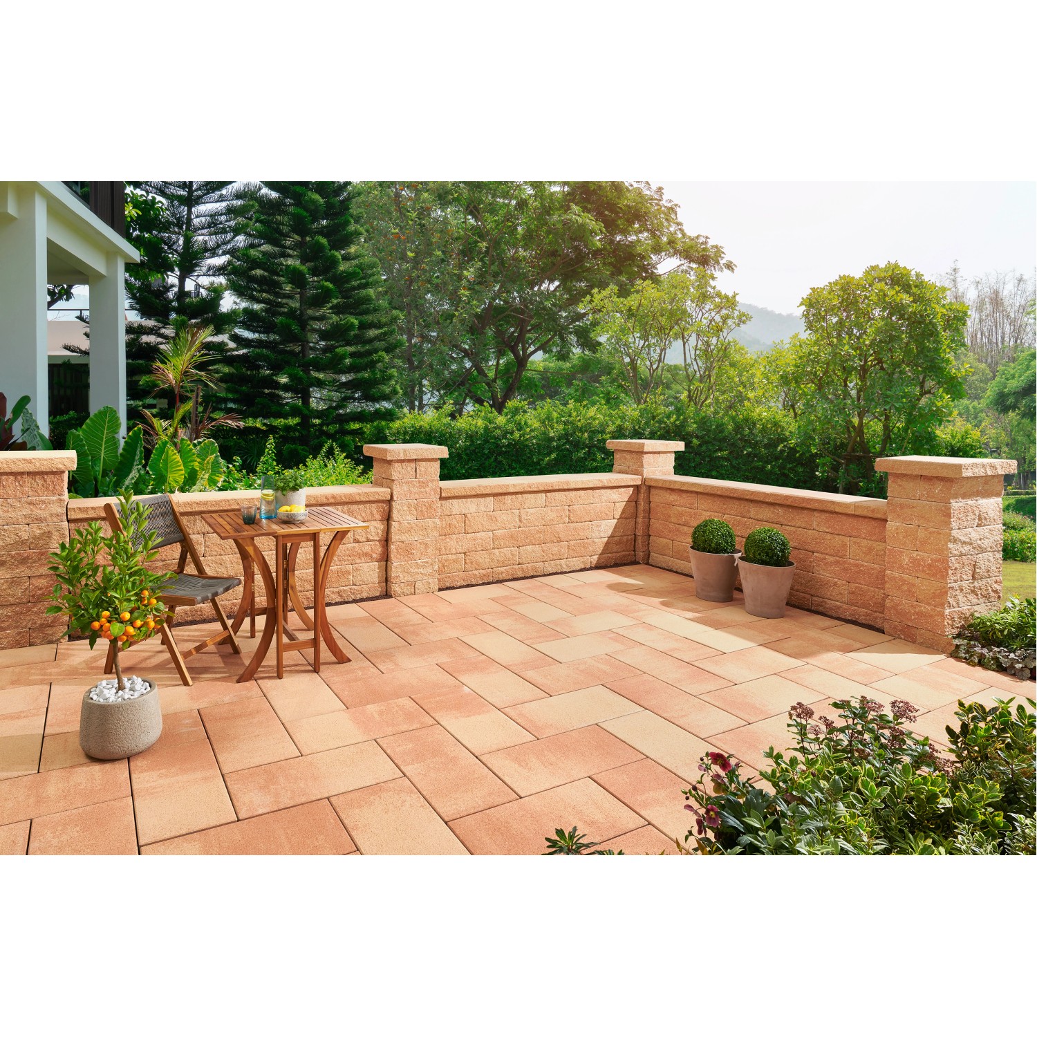 Bruchsteinmauer mit Pfeilerelementen in Sandsteinoptik, Teil einer Gartengestaltung mit Sitzbereich.