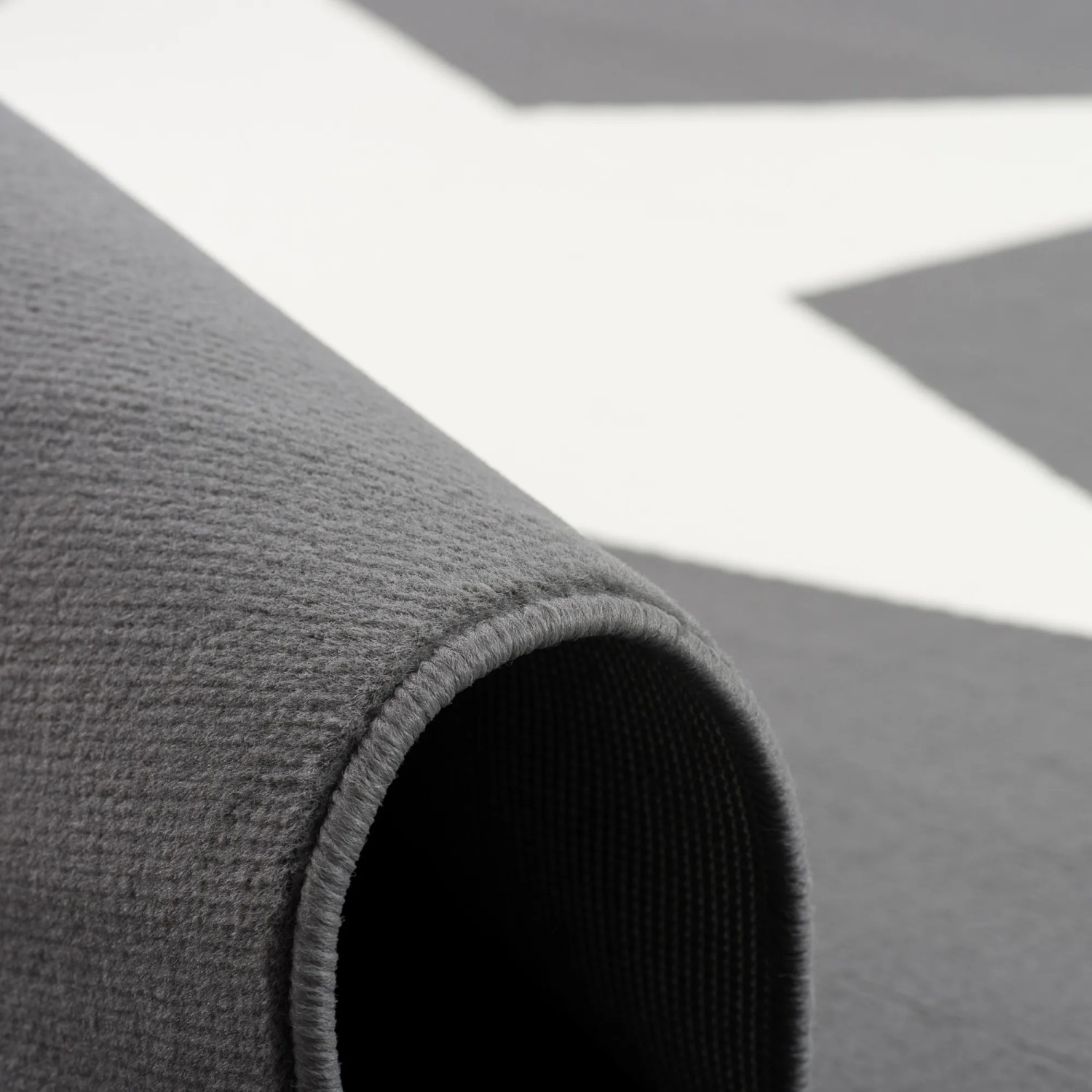 Nahaufnahme: Anthrazitfarbener Kinderteppich mit Sternmuster, gerollt.