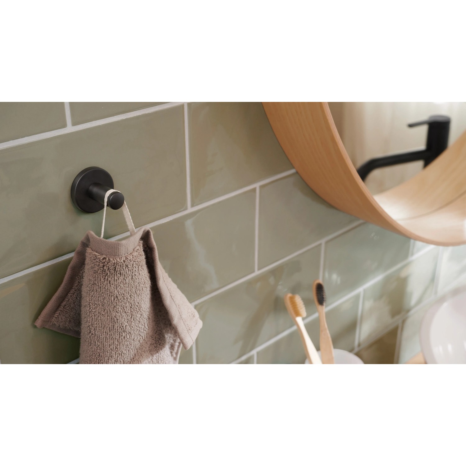 Tesa Handtuchhaken Moon, schwarz matt, mit Handtuch an grüner Wand. Rostfreier Handtuchhalter mit Klebelösung.