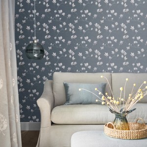Laura Ashley Vliestapete Magnolia Grove Dusky Seaspray im Wohnraum mit Sofa und Deko.