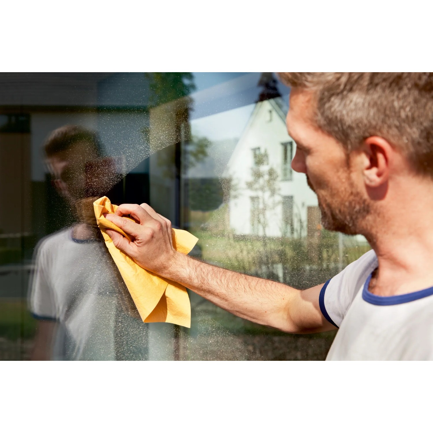 Mann reinigt Fenster mit gelbem Vileda Fenstertuch für streifenfreien Glanz.