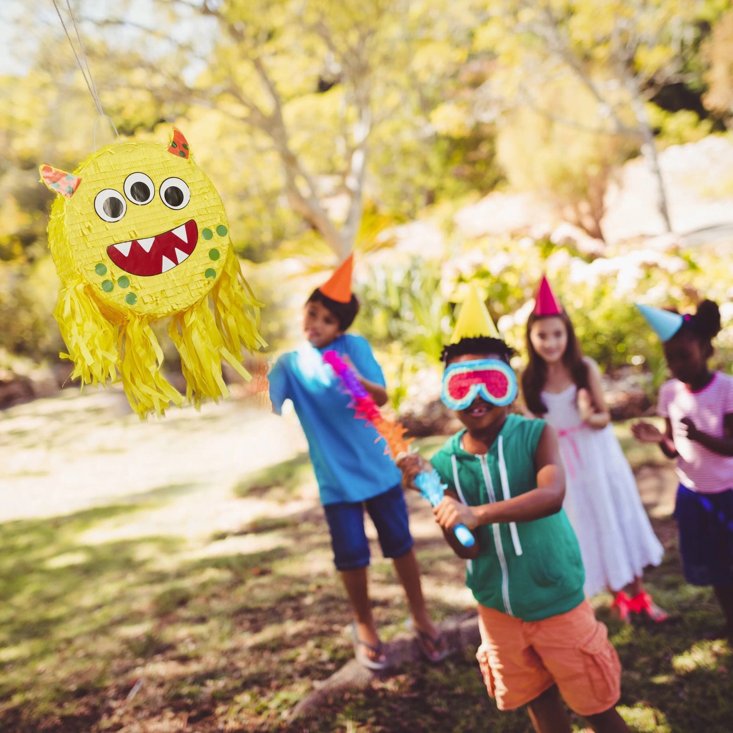 Gelbe Monster Pinata aus Pappe mit drei Augen hängt im Garten. Kinder spielen blindlings das Party-Spiel. Perfekt für Kindergeburtstage.