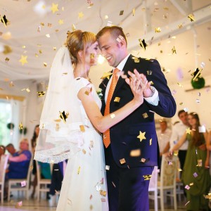 Glückliches Brautpaar tanzt unter goldenem Sternenregen Konfetti. Ideal für Hochzeit, Geburtstag, Party mit Partypopper.