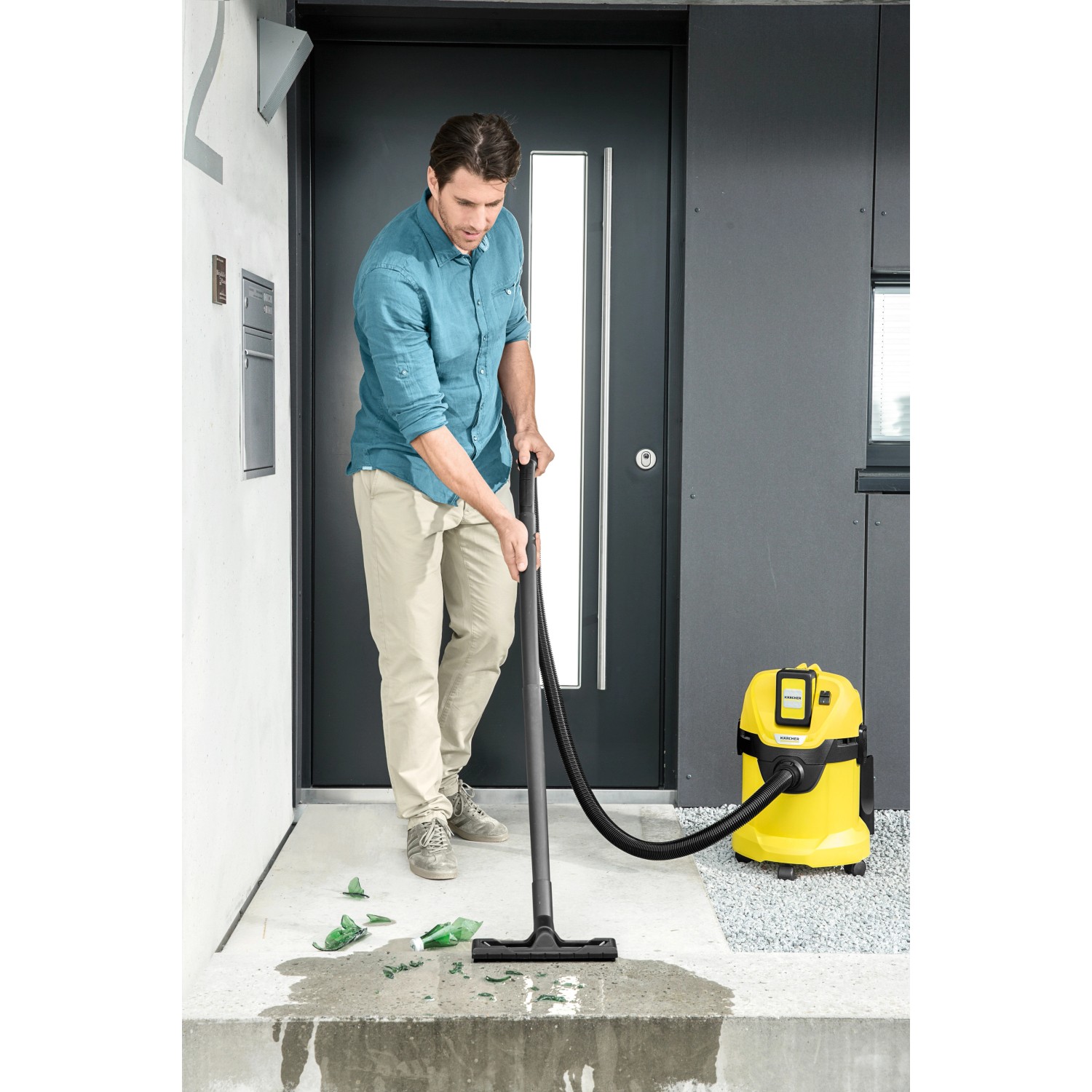 Mann saugt mit gelbem Kärcher Akku-Mehrzwecksauger WD 3 Glasscherben und Wasser vor einer Haustür.