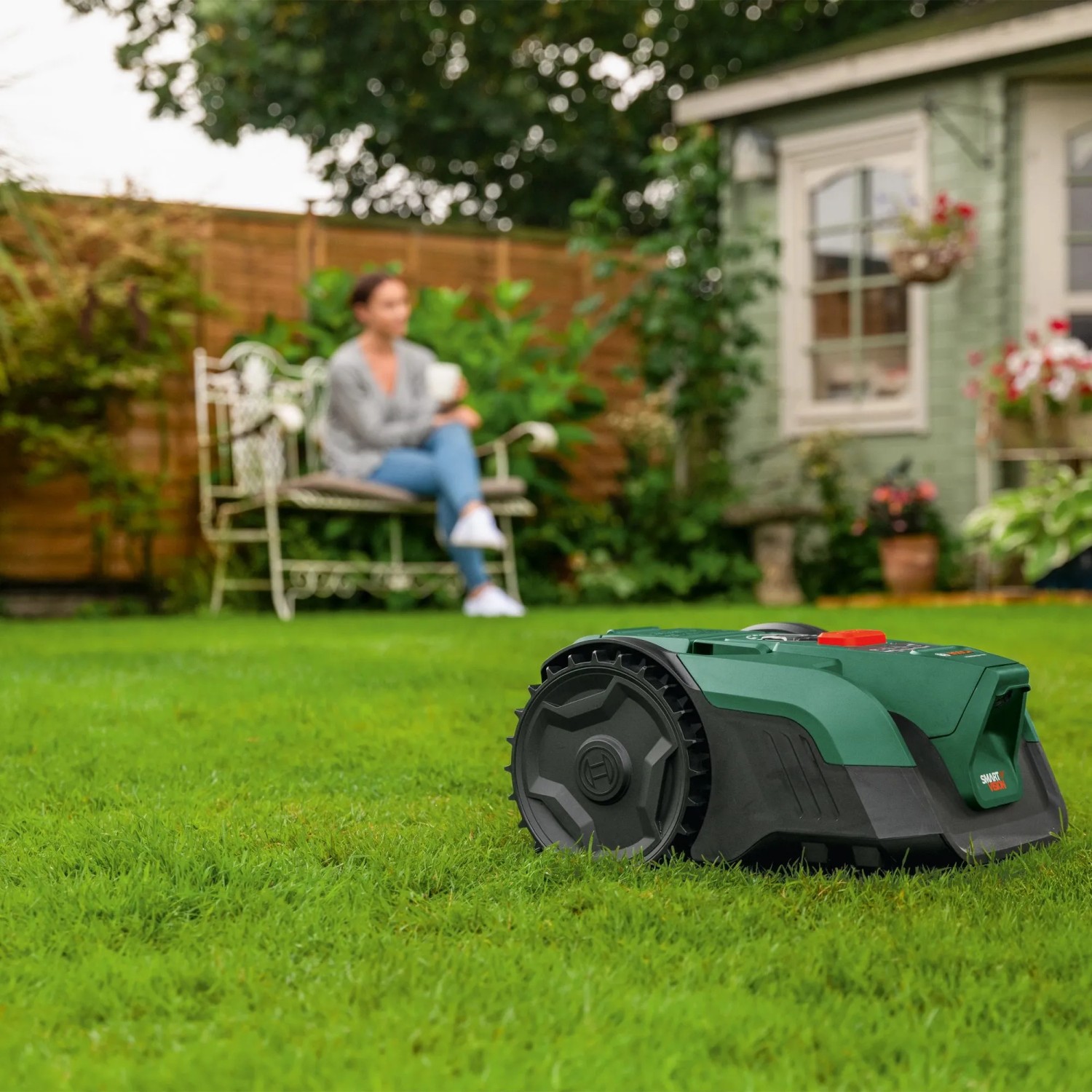 Bosch VISIMOW18V-100 Mähroboter auf Rasen, Frau im Hintergrund.