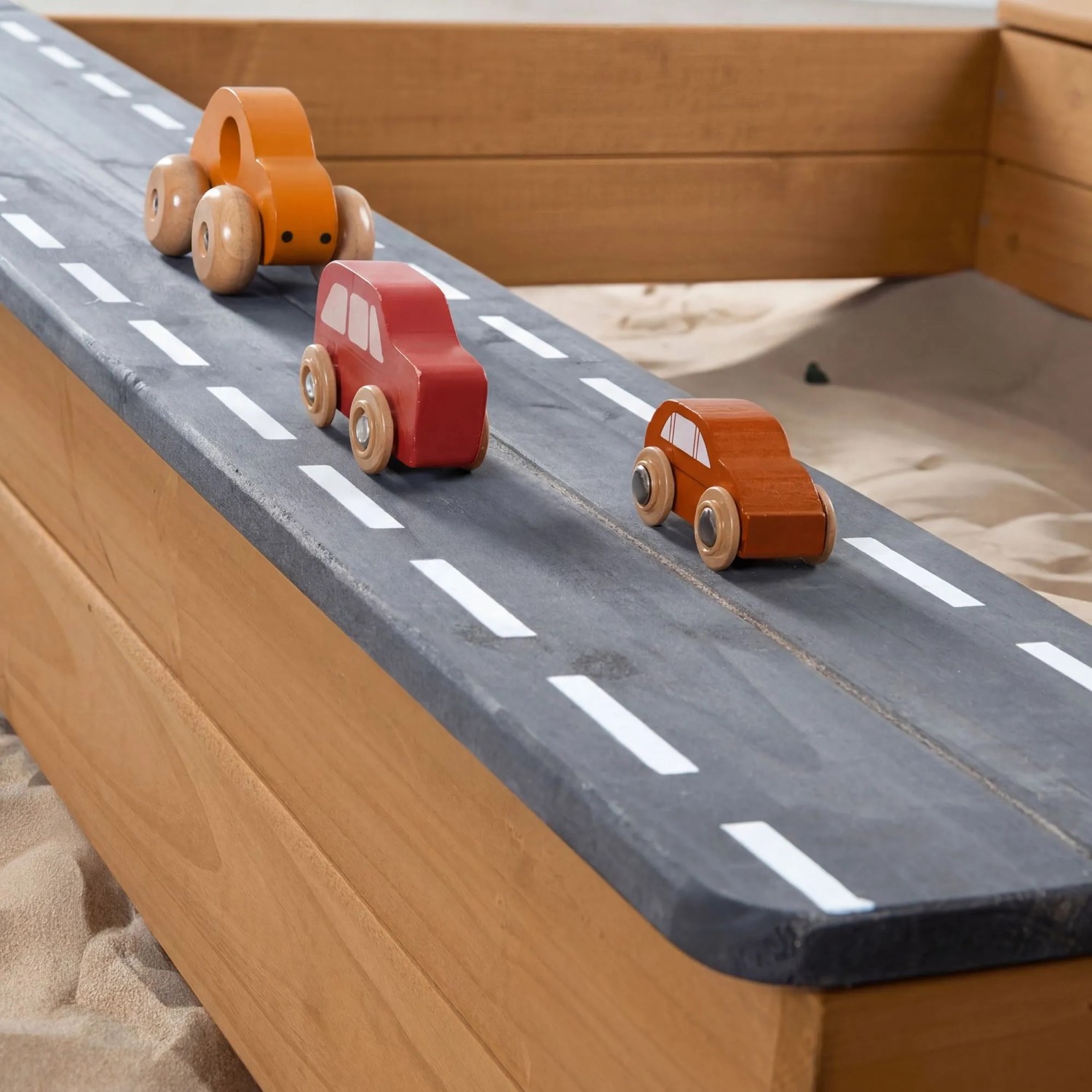 Roba Sandkasten: Detail der Holzstraße mit drei bunten Spielzeugautos. Ideal für fantasievolle Rollenspiele im Garten.