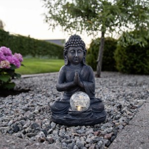 Graue LED-Solar-Buddha Figur mit bronzenen Akzenten, hält leuchtende Crackle-Glaskugel. Ideal für Garten und Terrasse.