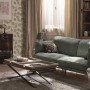 Wohnzimmer mit brauner Marburg Vliestapete GZSZ mit Blattmotiv, grünes Sofa und Holztisch.