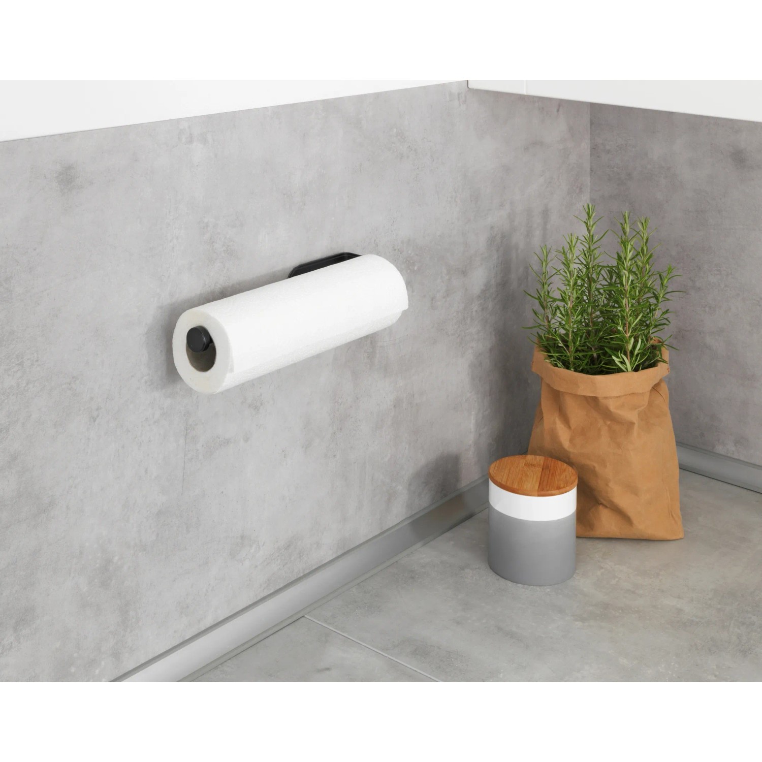 Wenko Küchenrollenhalter Nio, selbstklebend, schwarz, an grauer Wand mit Küchenrolle.