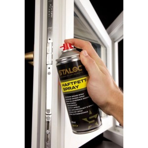 Hand sprüht Staloc Haftfettspray auf den silbernen Dreh-/Kippbeschlag eines weißen Fensters. Schützt Gelenke und Scharniere.