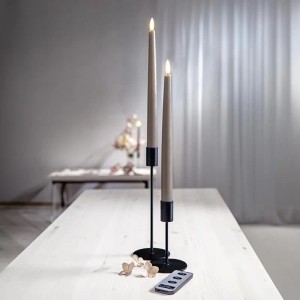 Zwei braune LED Stabkerzen aus Echtwachs mit warmweißer 3D Flamme und Fernbedienung auf Holztisch.